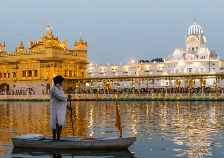 Visitor standing in a small boat on the sacred water near the illuminated Golden Temple in Amritsar, India.