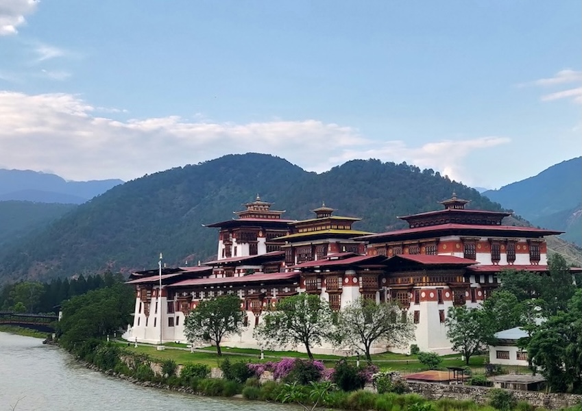 Traditional Bhutanese dzong beside a river with forested mountains in the background