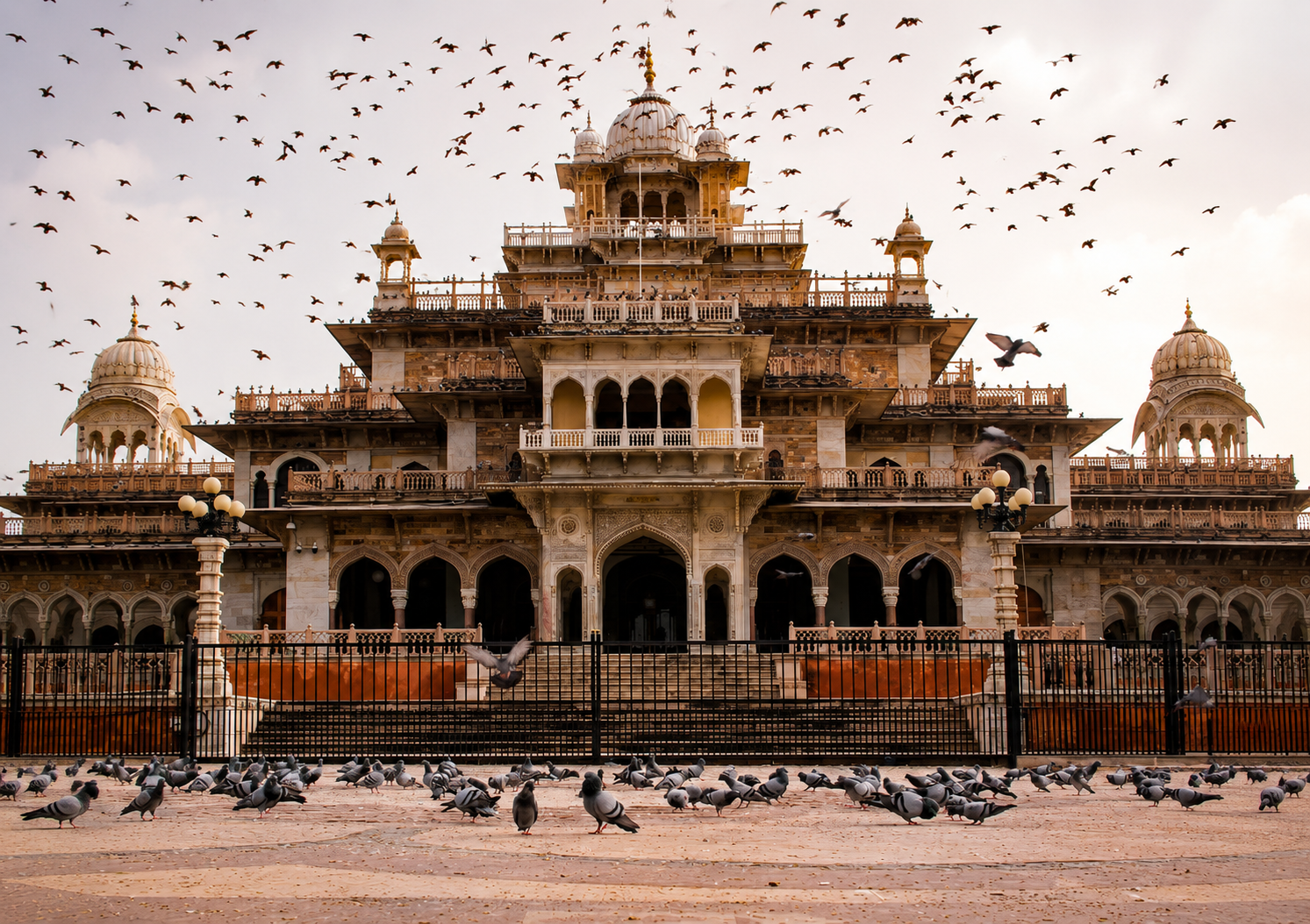 Historic Sikh architecture in Amritsar, India, with pigeons on the ground and birds flying overhead.