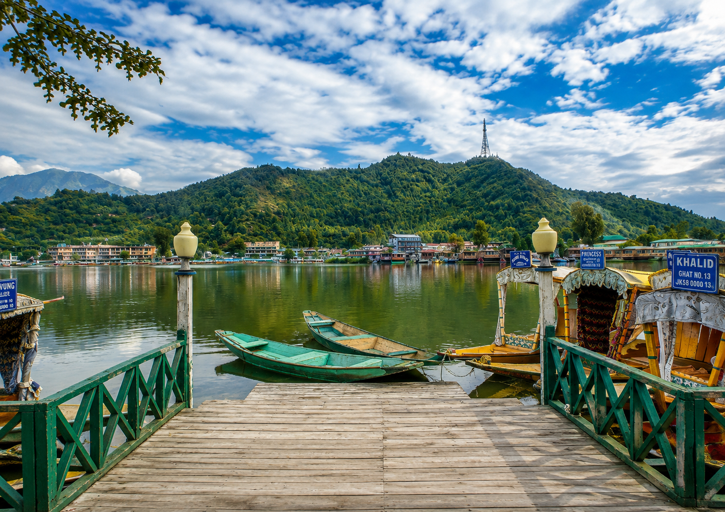 Dal Lake Kashmir with traditional shikaras, wooden dock, and green mountains in the background