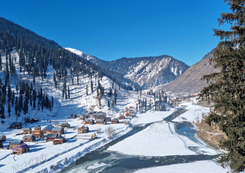 Snowy Kashmir village with a river, pine trees, and mountain landscape in winter