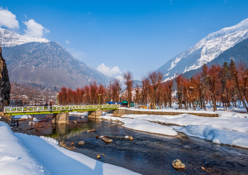 Snowy river in Kashmir with a bridge, trees, and Himalayan mountains in the background