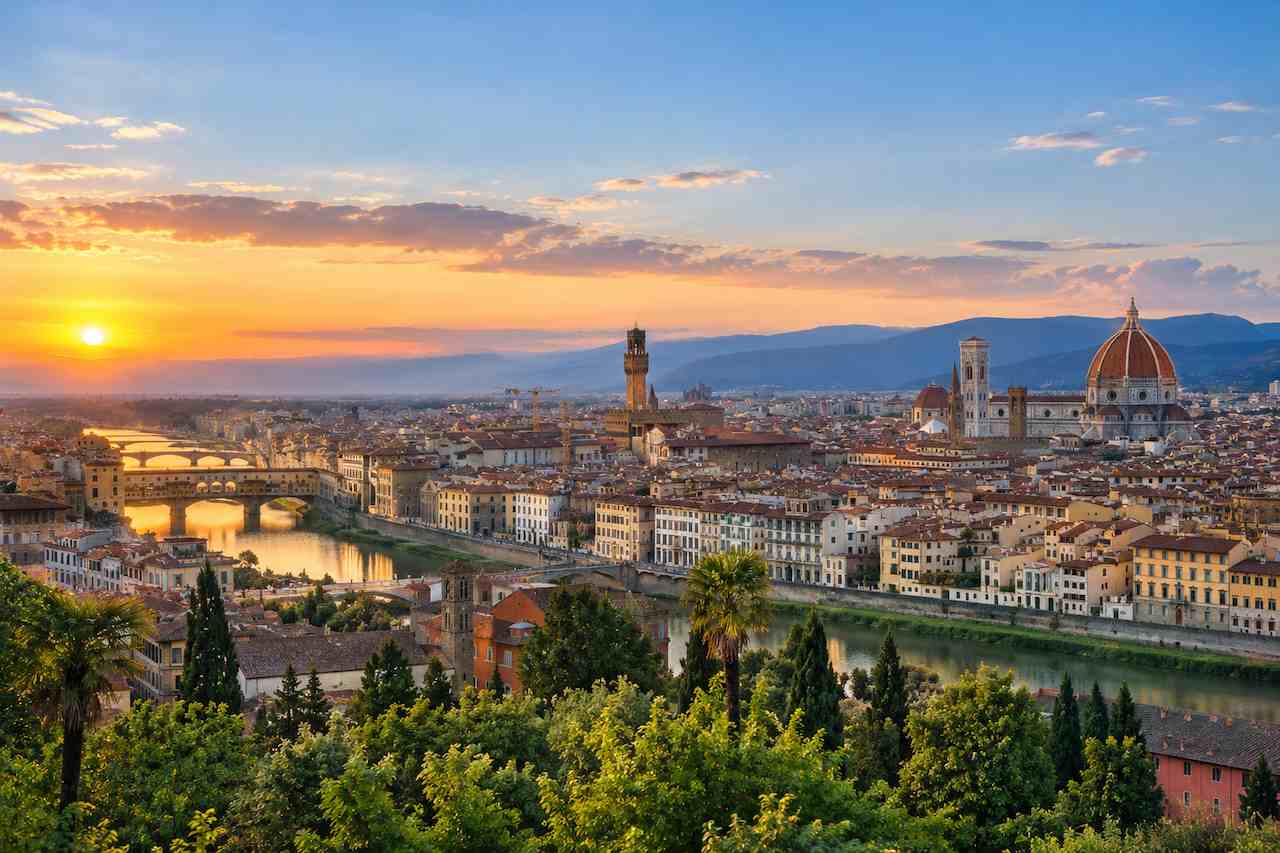Panoramic view of Florence, Italy, featuring the Arno River, historic bridges, Florence Cathedral, and scenic city skyline at sunset.